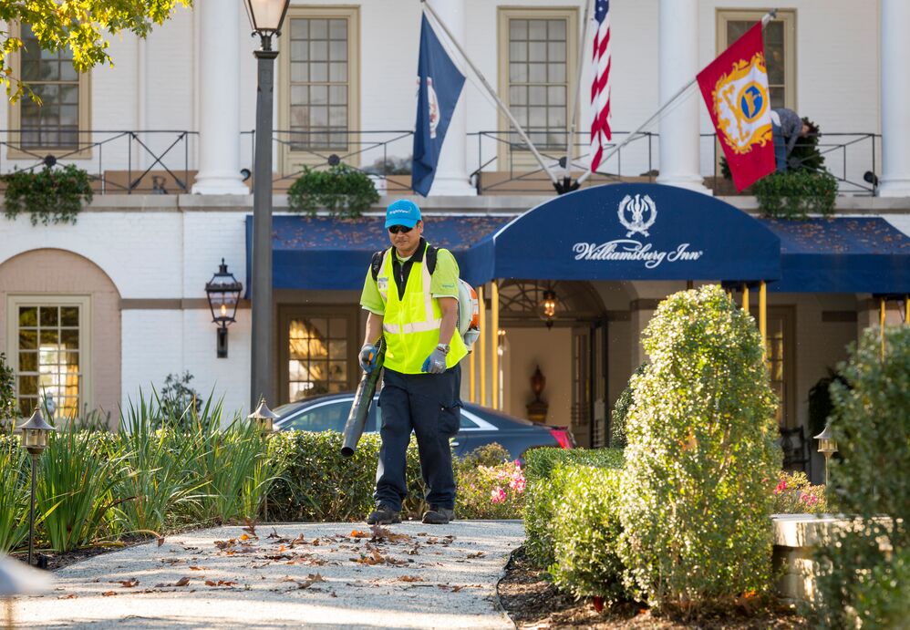 landscape maintenance crew member blowing leaves off walkway